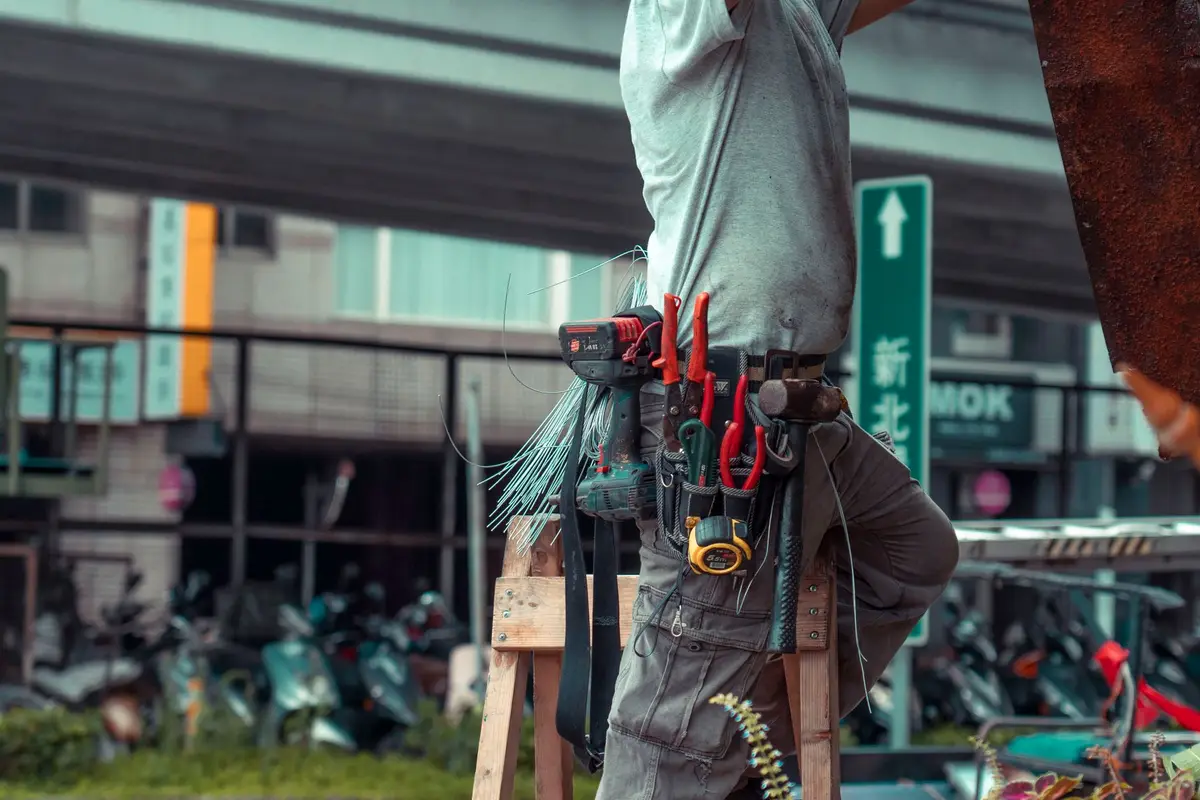 Contractor on a ladder with a tool belt working on a house exterior