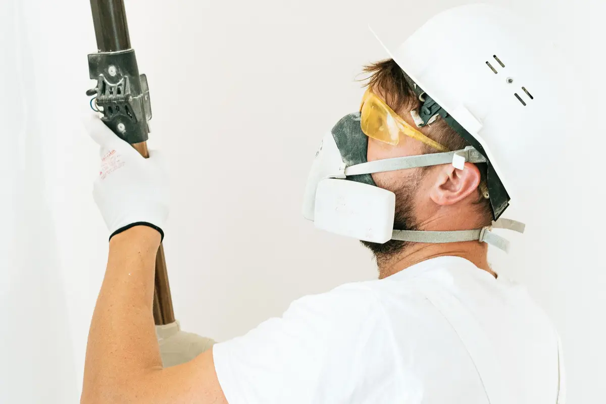 Painter in safety gear rolling paint onto an interior wall